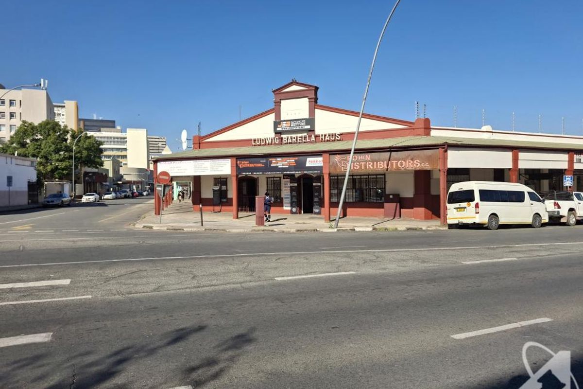 Street-level view of Ludwig Barella Haus, a commercial building featuring a gabled roof, covered veranda, and prominent street-facing signage.