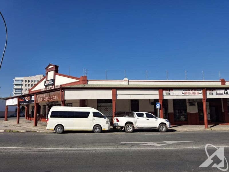 Front elevation of a commercial building featuring a covered walkway, security fencing, and prominent signage for multiple business tenants.