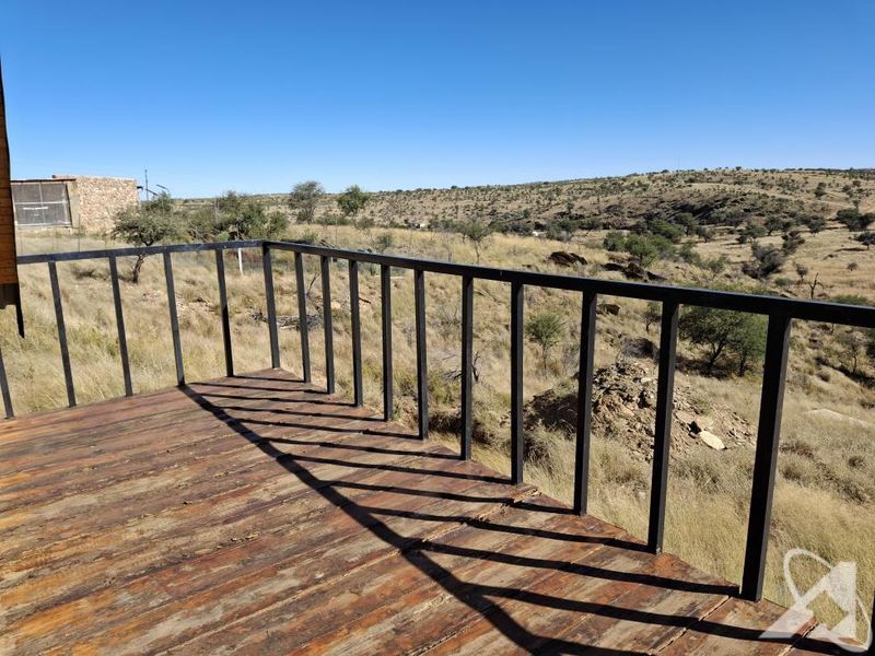 An elevated timber deck featuring a black metal railing, offering expansive views of the surrounding rural landscape.