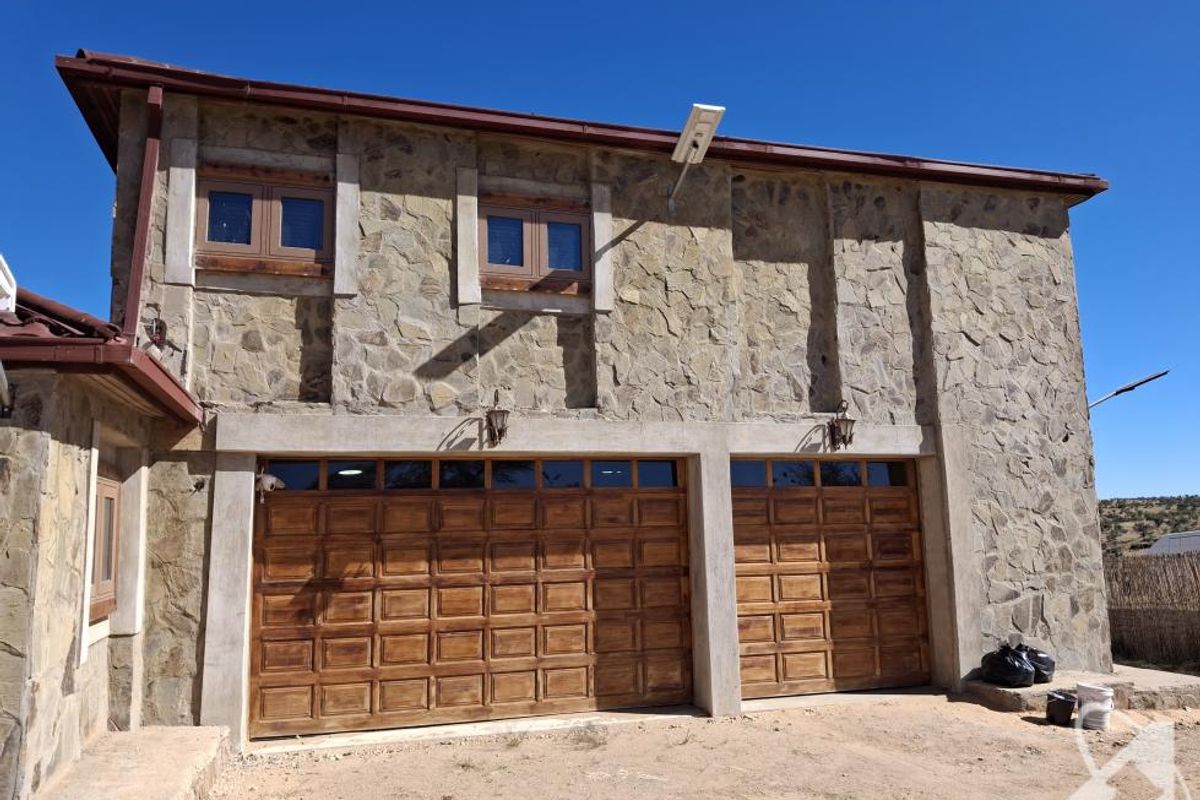 A double garage featuring stone cladding, timber-framed windows, and wooden garage doors, set against a clear sky.