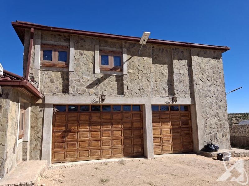 A double garage featuring stone cladding, timber-framed windows, and wooden garage doors, set against a clear sky.