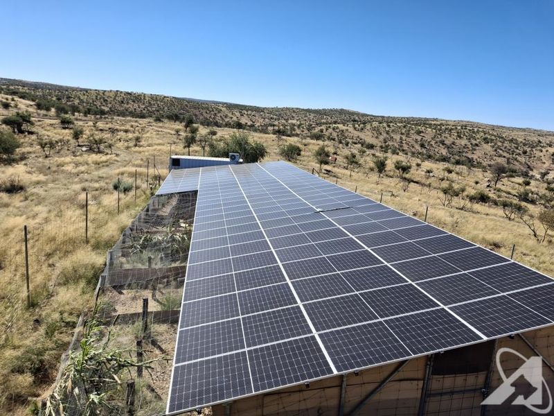 An elevated view of a large solar panel array installed on a utility structure within a rural small holding landscape.