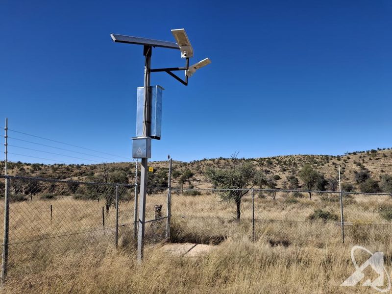 A solar-powered security camera system mounted on a utility pole within a fenced perimeter on the small holding.