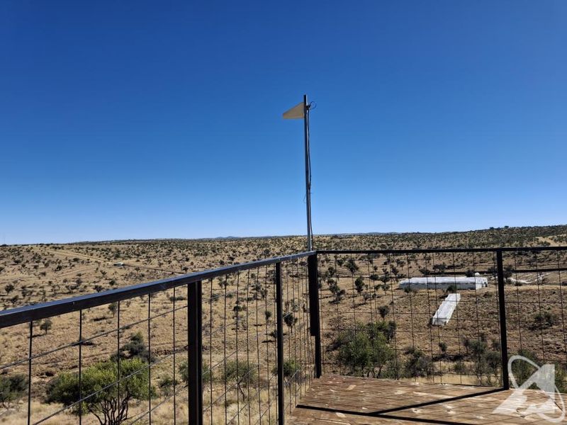 An elevated balcony with metal railings and wooden decking, offering expansive views of the surrounding arid landscape.