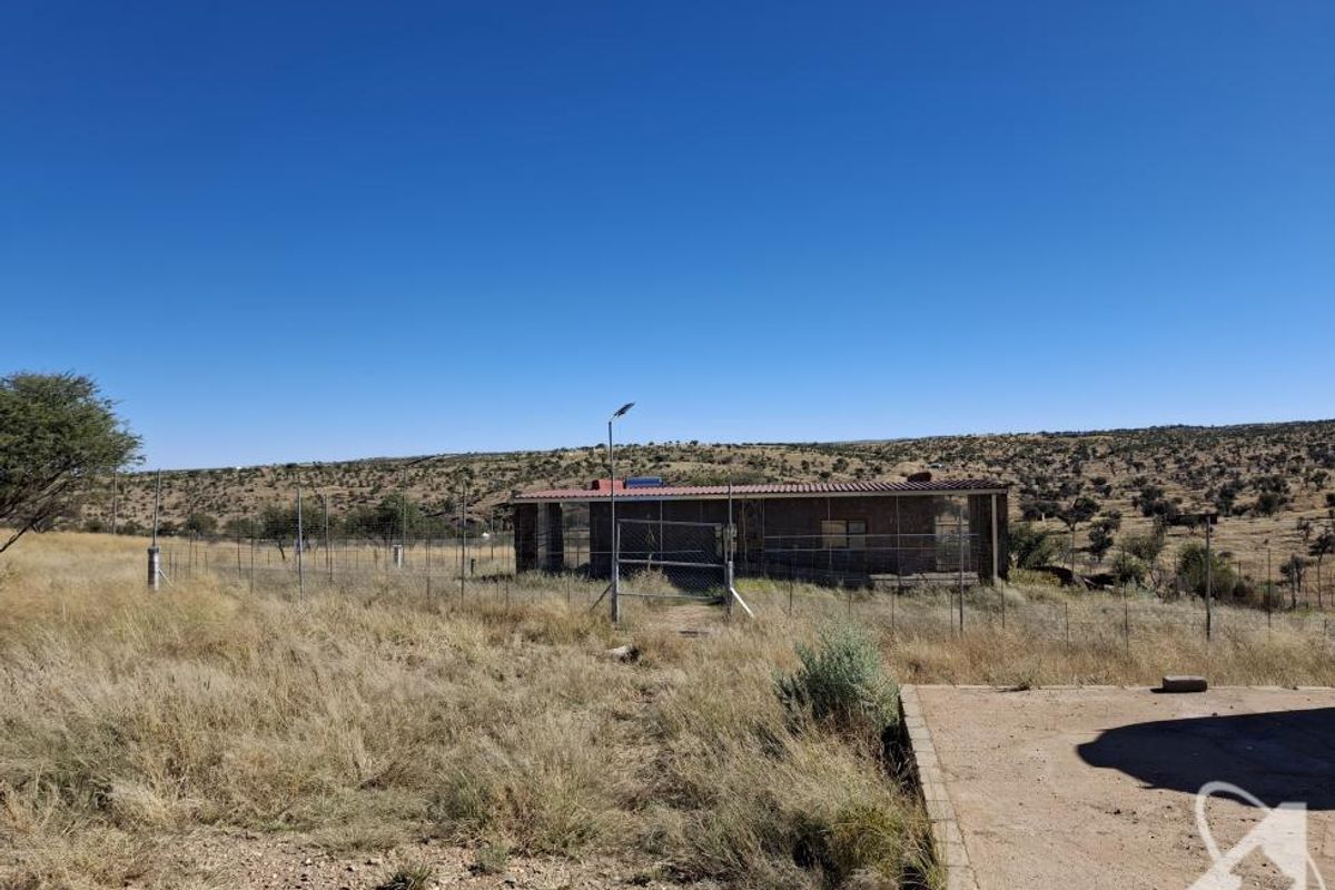 A view of the rear exterior of the property featuring a fenced perimeter, concrete apron, and surrounding dry landscape.
