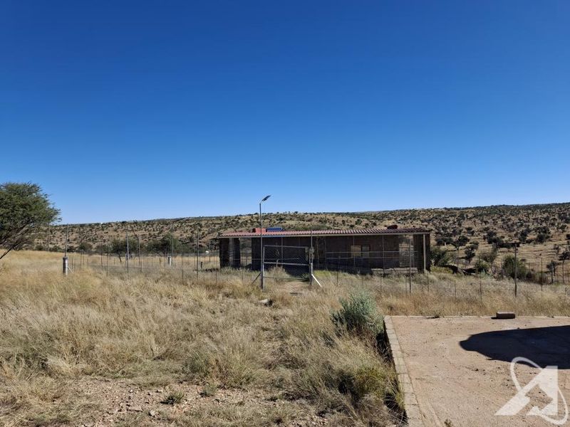 A view of the rear exterior of the property featuring a fenced perimeter, concrete apron, and surrounding dry landscape.