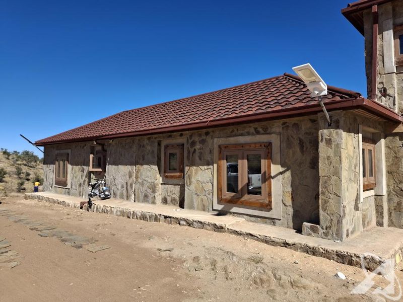 Exterior view of a stone-clad building featuring a tiled roof, wooden window frames, and an integrated solar security light.