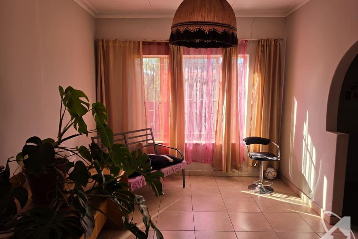 A living room area featuring tiled flooring, a large window with natural light, and an arched entryway, showing signs of minor structural cracking.