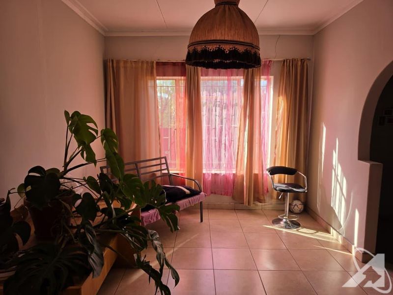 A living room area featuring tiled flooring, a large window with natural light, and an arched entryway, showing signs of minor structural cracking.