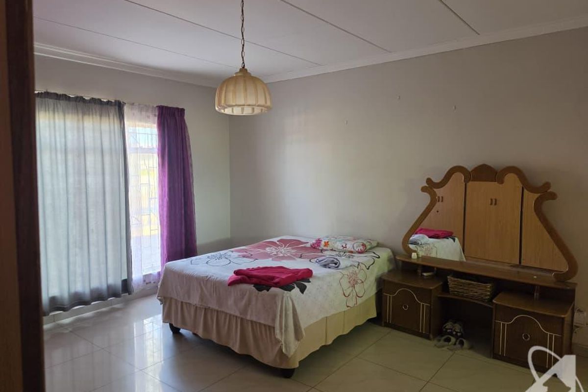 A spacious bedroom featuring tiled flooring, a central pendant light fixture, and large windows with curtain rails.
