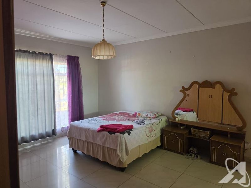 A spacious bedroom featuring tiled flooring, a central pendant light fixture, and large windows with curtain rails.