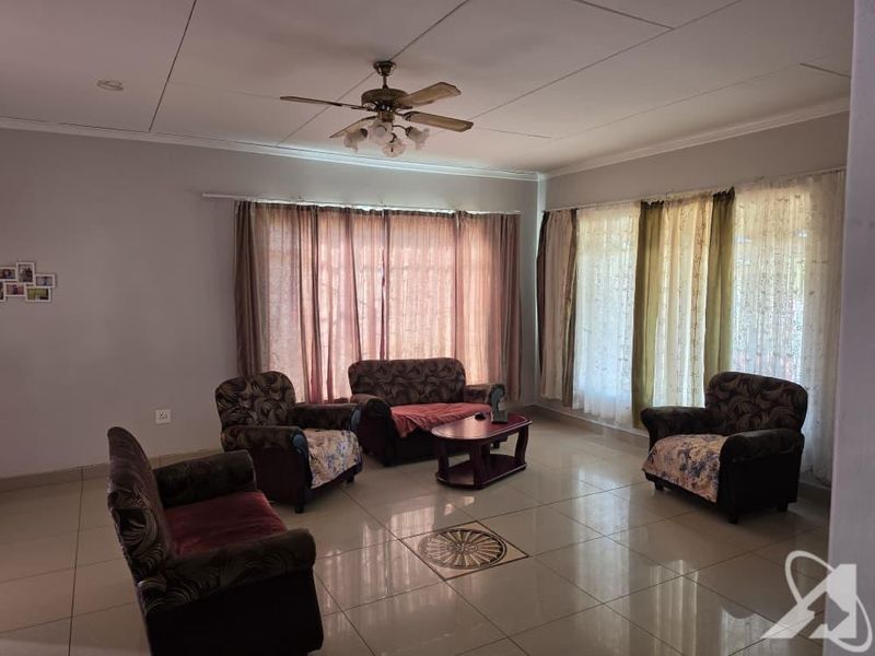 Spacious living room featuring large windows, tiled flooring, and a ceiling fan, offering a bright and functional space for relaxation.