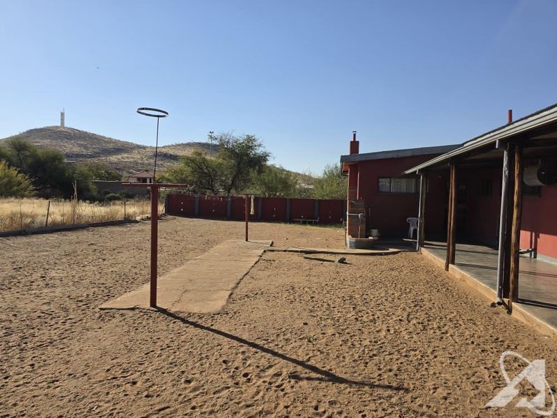 Rear exterior view showing a covered patio, sandy yard area, perimeter wall, and outdoor washing line with mountain views in the background.