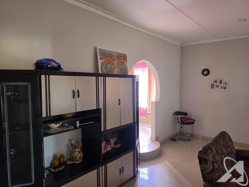 A living area featuring tiled flooring, a coved ceiling, and an arched doorway leading to an adjacent space.
