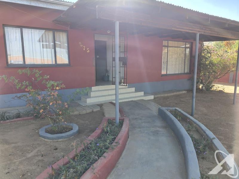 Front elevation of a house featuring a covered porch, tiled entrance steps, security gate, and a concrete walkway with raised garden beds.