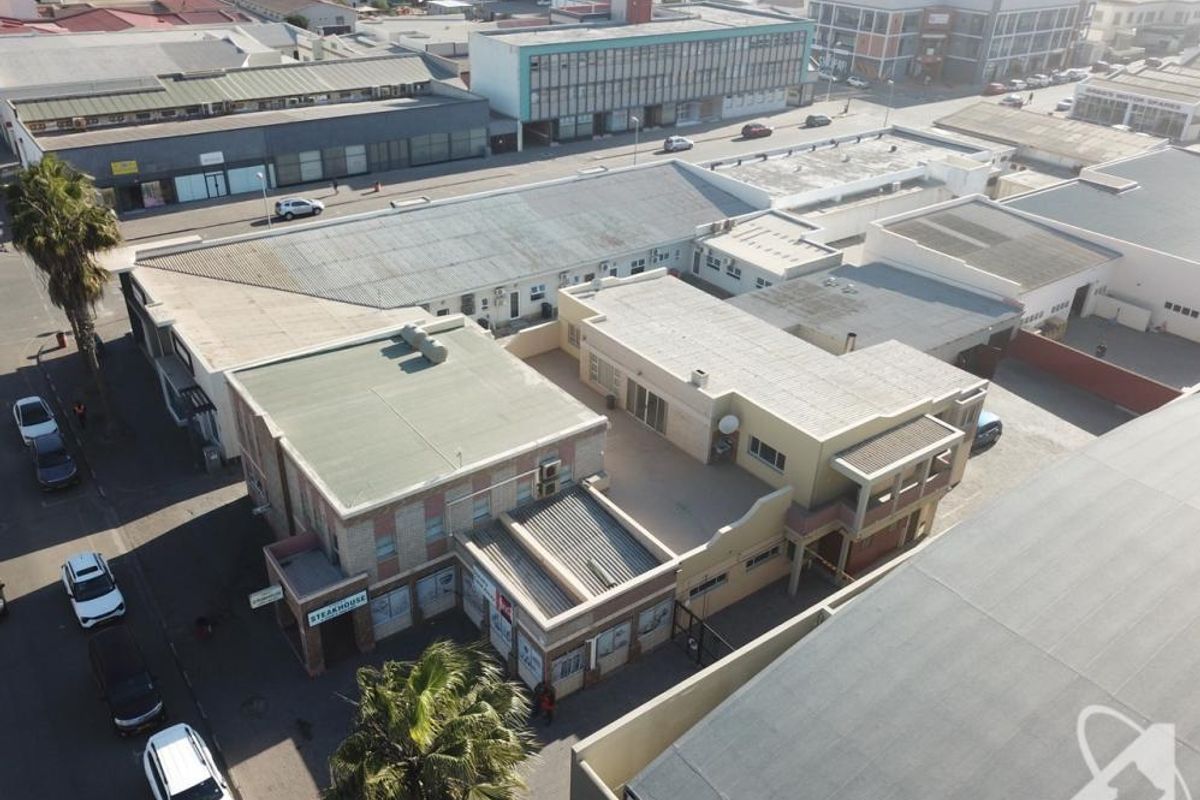 Aerial view of a commercial property complex featuring flat roofs, paved courtyard areas, and street-level storefronts in an urban setting.