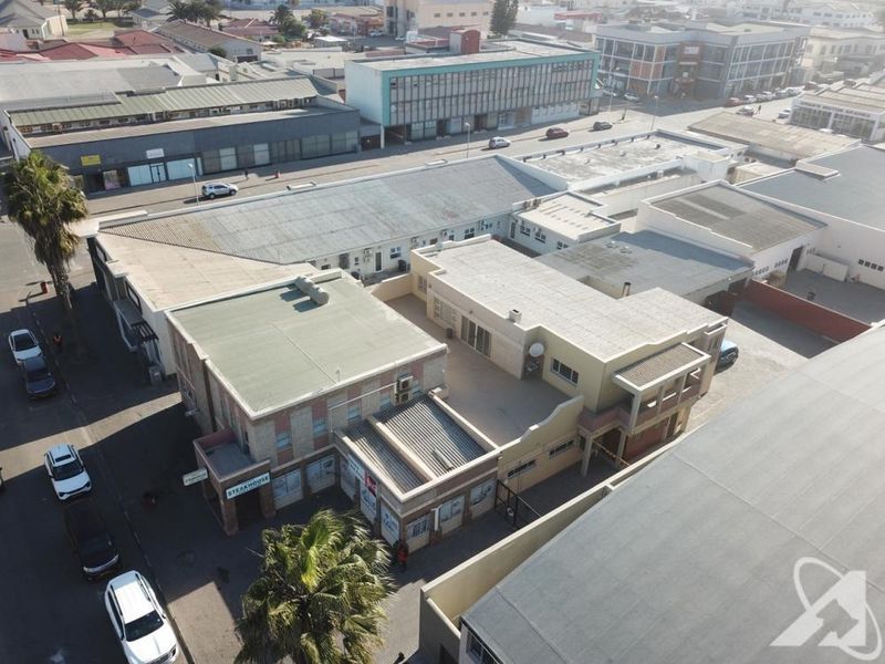 Aerial view of a commercial property complex featuring flat roofs, paved courtyard areas, and street-level storefronts in an urban setting.