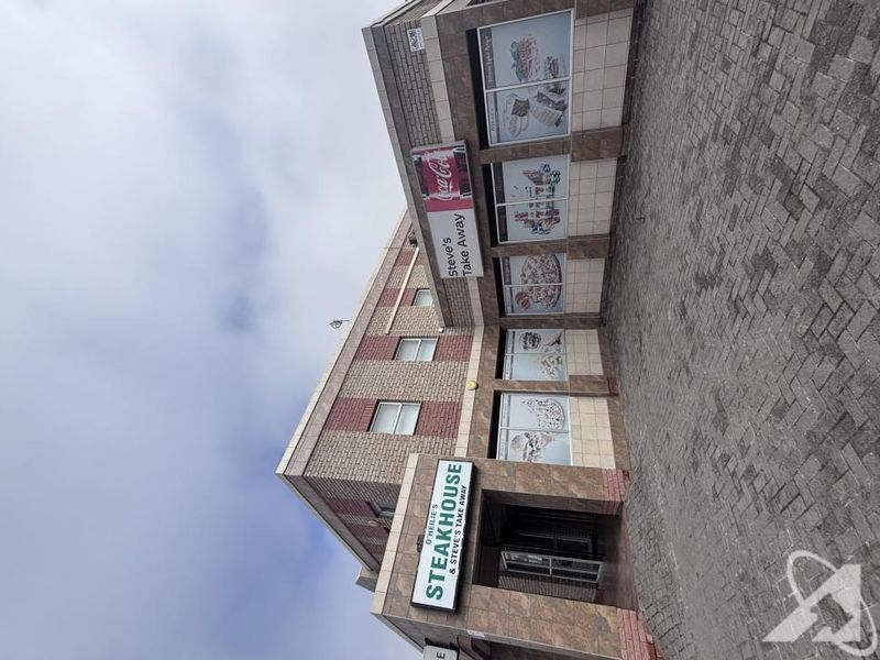 Front exterior view of a commercial building featuring brick and tiled facade, large display windows, and paved entrance area.