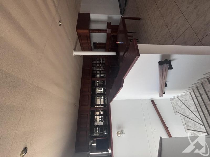 A commercial bar area featuring built-in wooden cabinetry and counter space, adjacent to a staircase with a wooden handrail and tiled flooring.