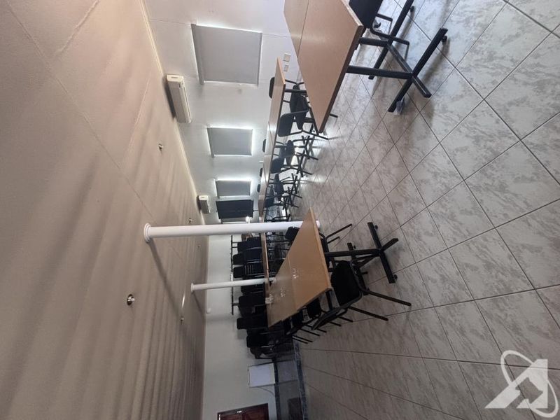 A functional commercial office space featuring tiled flooring, structural support columns, and wall-mounted air conditioning units, suitable for a meeting or training room setup.