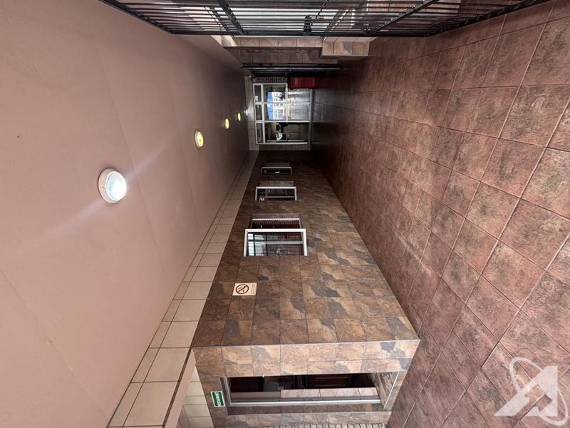 A covered exterior walkway featuring tiled wall cladding, recessed lighting, and a secure metal gate entrance.
