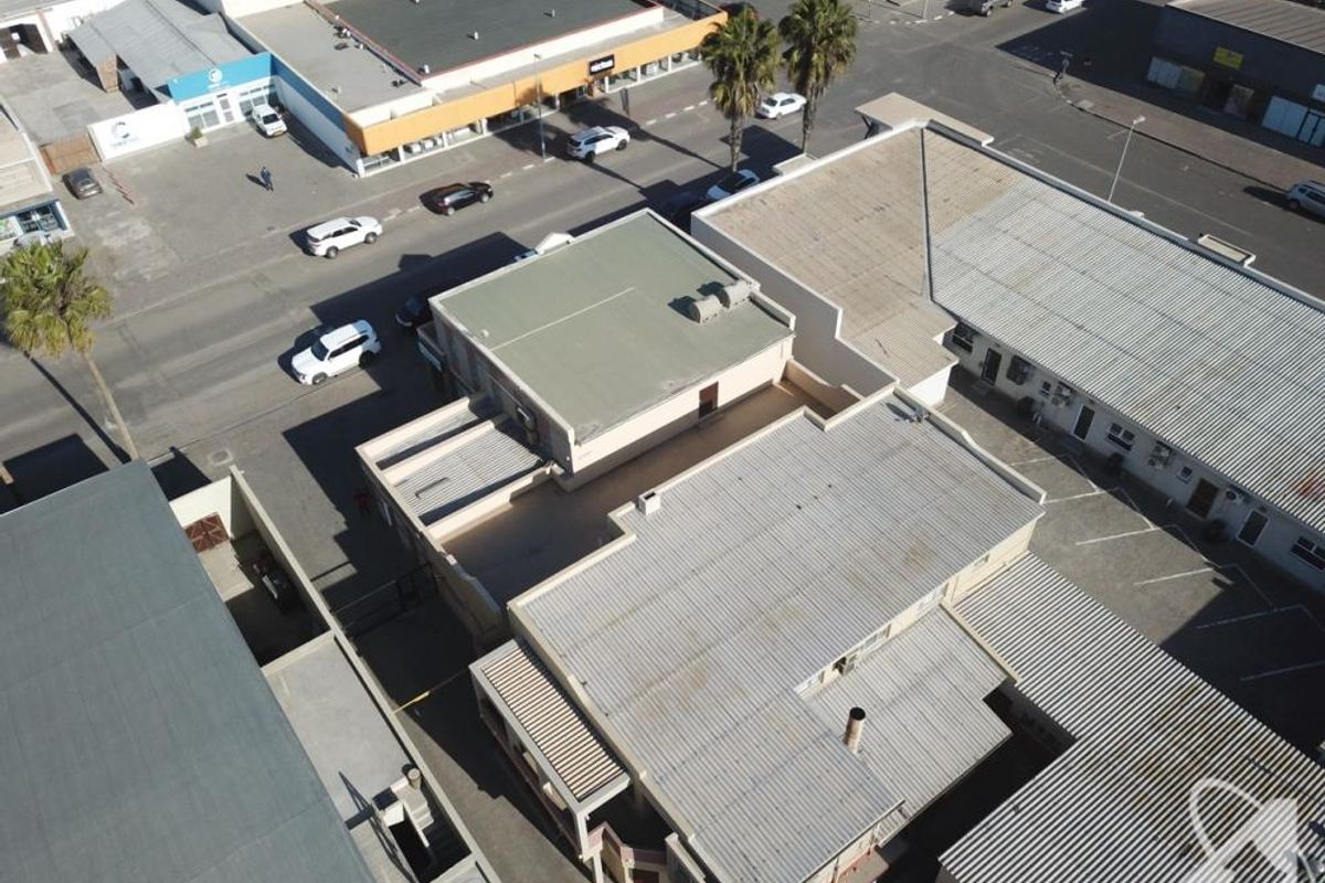Aerial view of a commercial property complex featuring corrugated metal roofing, flat roof sections, and adjacent asphalt parking areas.