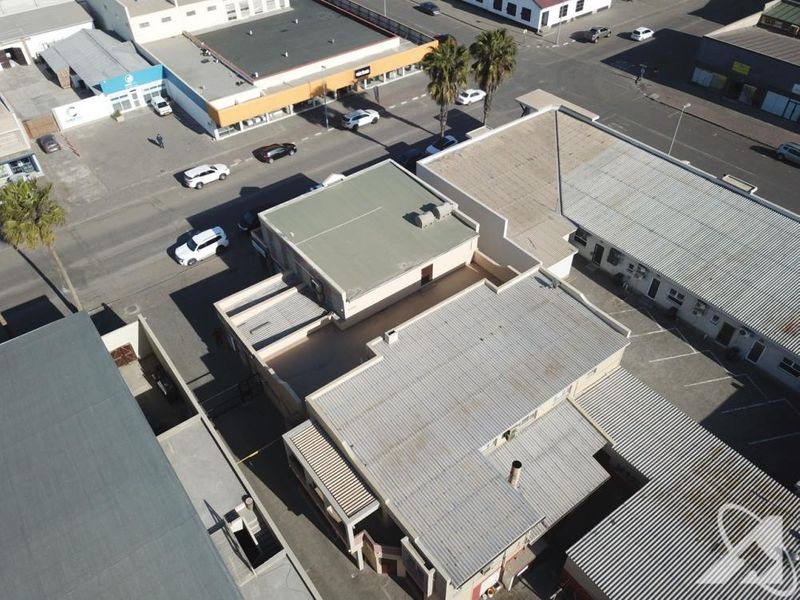 Aerial view of a commercial property complex featuring corrugated metal roofing, flat roof sections, and adjacent asphalt parking areas.