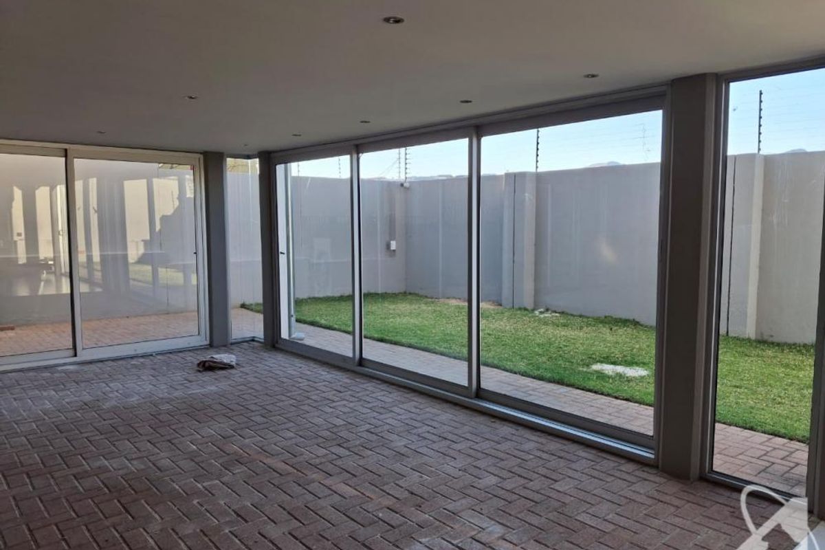 A spacious, covered patio area featuring large sliding glass doors, recessed lighting, and paved flooring, overlooking a private enclosed garden.