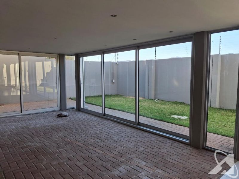 A spacious, covered patio area featuring large sliding glass doors, recessed lighting, and paved flooring, overlooking a private enclosed garden.