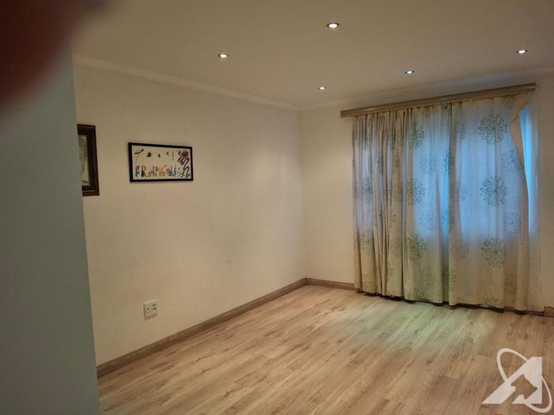 A bright, empty bedroom featuring modern laminate flooring, recessed downlighting, and neutral wall finishes, ready for personalization.