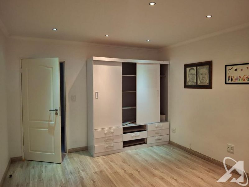 A bedroom featuring laminate flooring, recessed downlighting, and a built-in wardrobe with some missing drawer components.