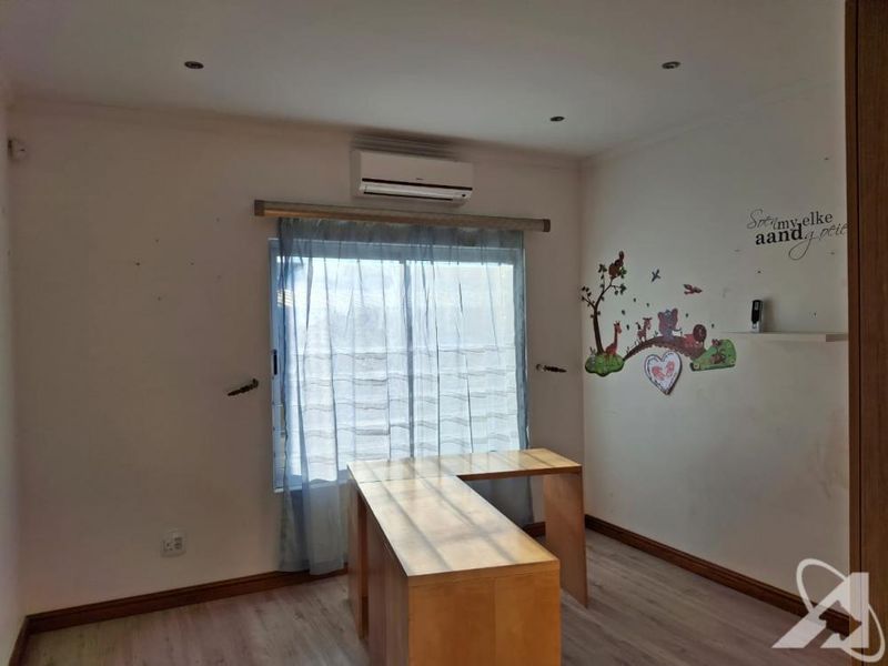 A bedroom featuring laminate flooring, recessed downlights, and a wall-mounted air conditioning unit.
