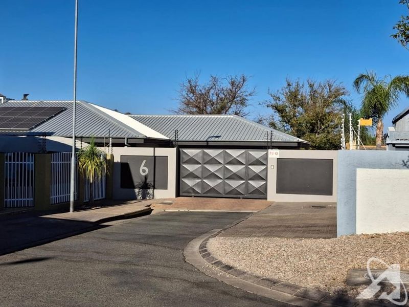 Front exterior view of the property featuring a modern metal roof with solar panels, secure boundary wall, and a large sliding driveway gate.
