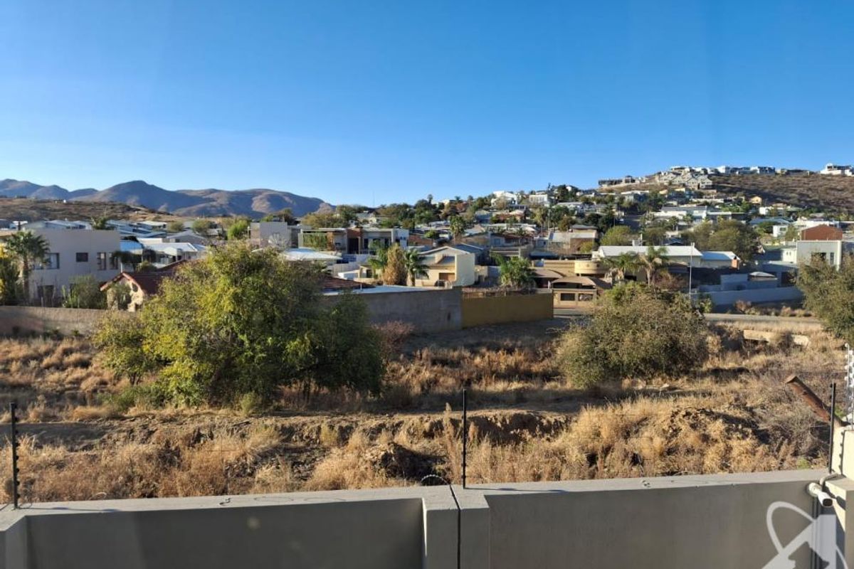 Elevated view overlooking the surrounding neighbourhood and distant hills, featuring a concrete boundary wall with integrated electric fencing in the foreground.