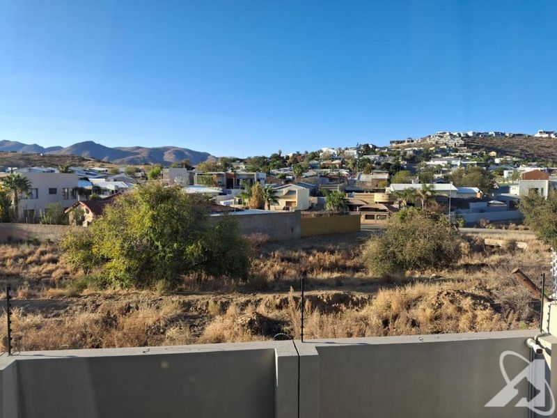 Elevated view overlooking the surrounding neighbourhood and distant hills, featuring a concrete boundary wall with integrated electric fencing in the foreground.