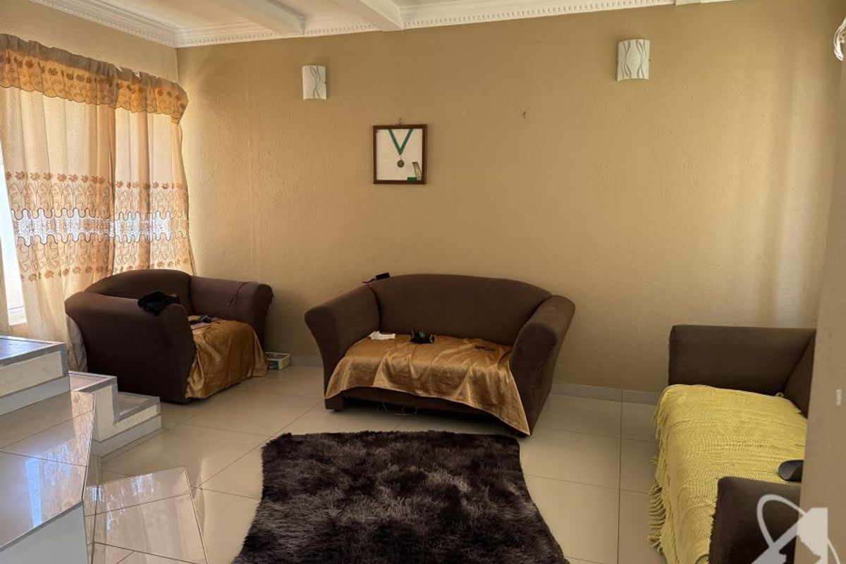 A spacious living room featuring tiled flooring, recessed ceiling lighting, and a raised platform area, providing a functional and comfortable living space.