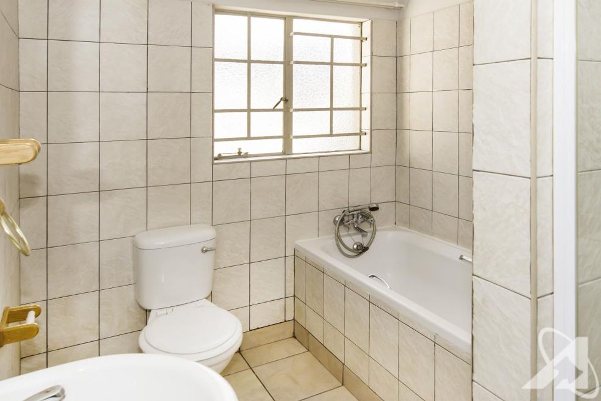 A functional bathroom featuring a built-in bathtub with shower mixer, a standard toilet, and tiled walls and flooring.