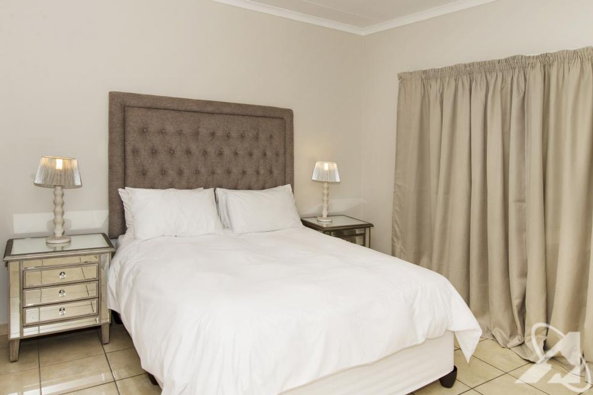 A well-maintained bedroom featuring neutral wall tones, tiled flooring, and full-length curtains.