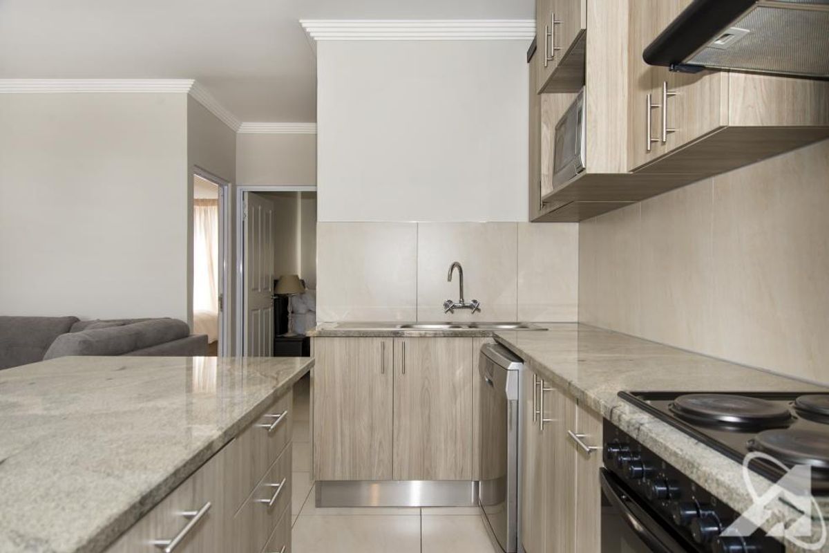 Modern kitchen featuring light wood cabinetry, granite countertops, integrated stove and extractor fan, and tiled flooring, seamlessly flowing into the living area.