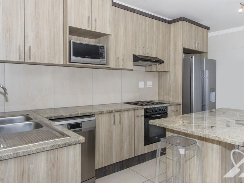 Modern kitchen featuring light wood-grain cabinetry, granite countertops, integrated appliances, and a functional breakfast island with tiled flooring.