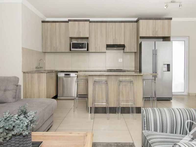 Modern open-plan kitchen featuring light wood cabinetry, a central island, and tiled flooring, seamlessly integrated with the living area.
