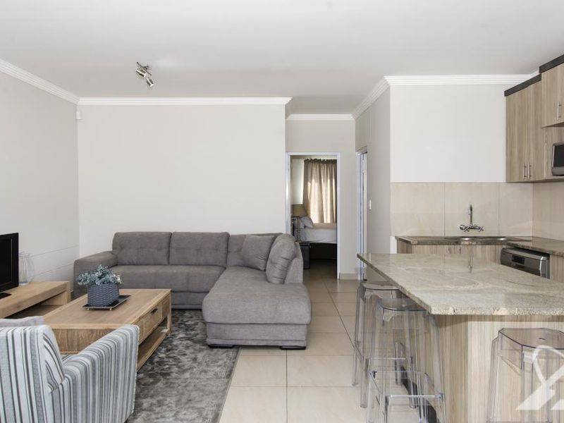 An open-plan living area featuring a modern kitchen with granite countertops, built-in cabinetry, and tiled flooring, seamlessly flowing into the lounge space.