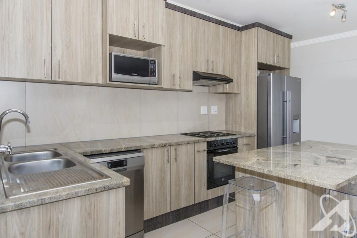 Modern kitchen featuring light wood-grain cabinetry, granite countertops, a double sink, built-in oven, hob, extractor fan, and integrated microwave space.