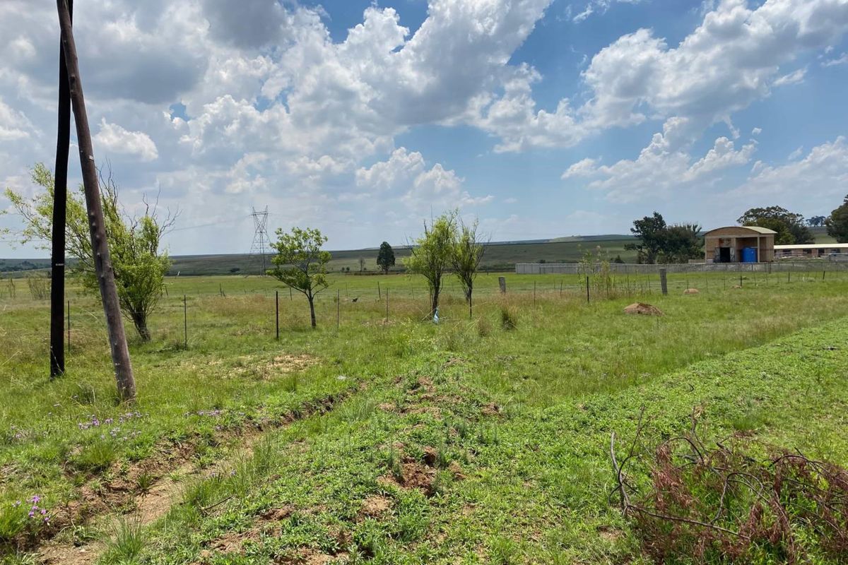 A view of the vacant residential land featuring open grassy terrain, perimeter fencing, and distant utility infrastructure under a clear sky.