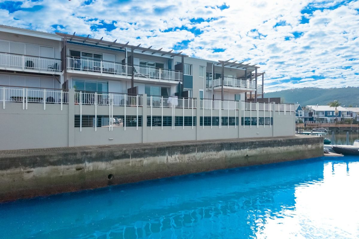 Exterior view of a waterfront apartment complex featuring private balconies with white railings and a concrete retaining wall along the water edge.