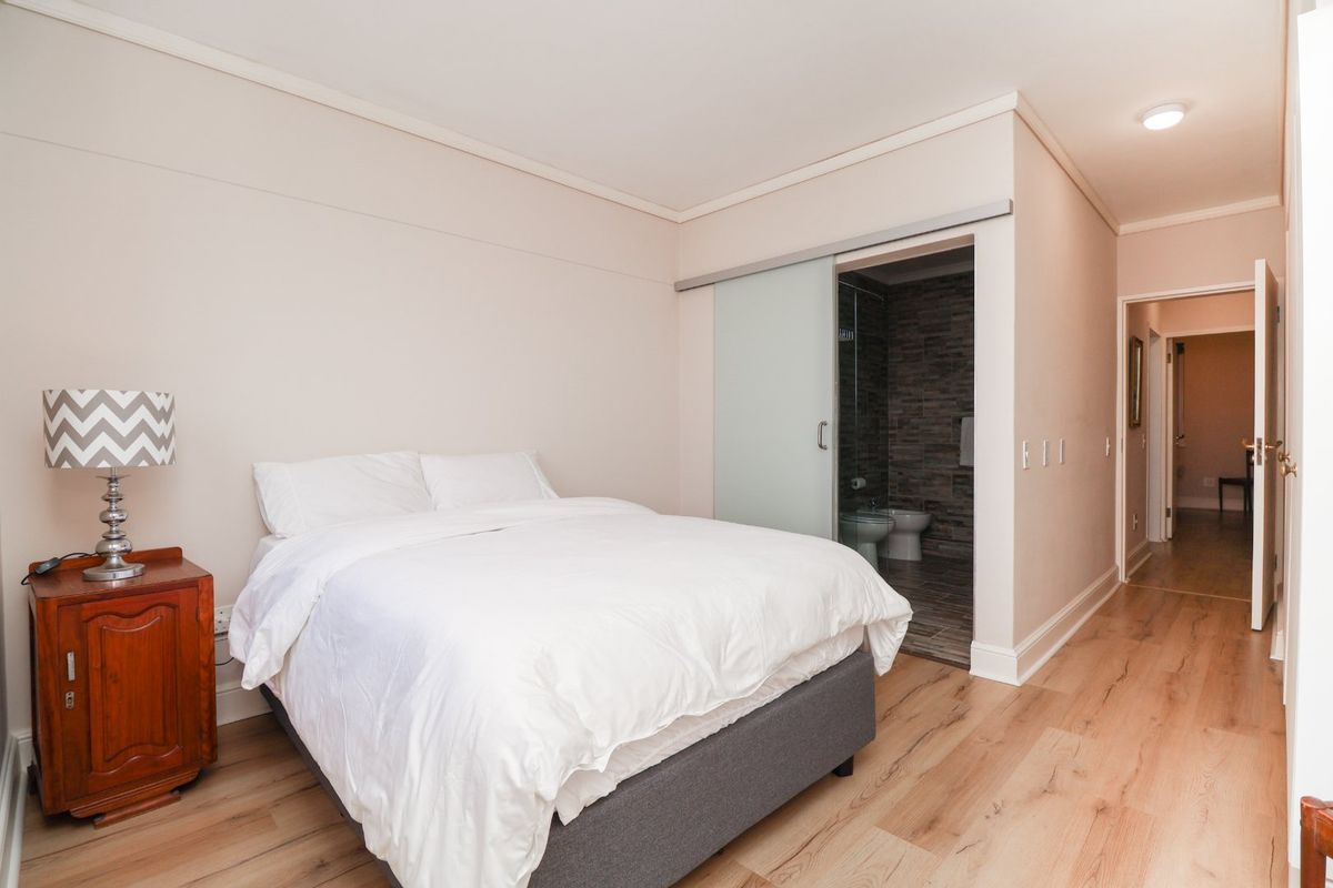 A well-maintained bedroom featuring light wood-look flooring, a sliding frosted glass door leading to an en-suite bathroom, and neutral wall finishes.