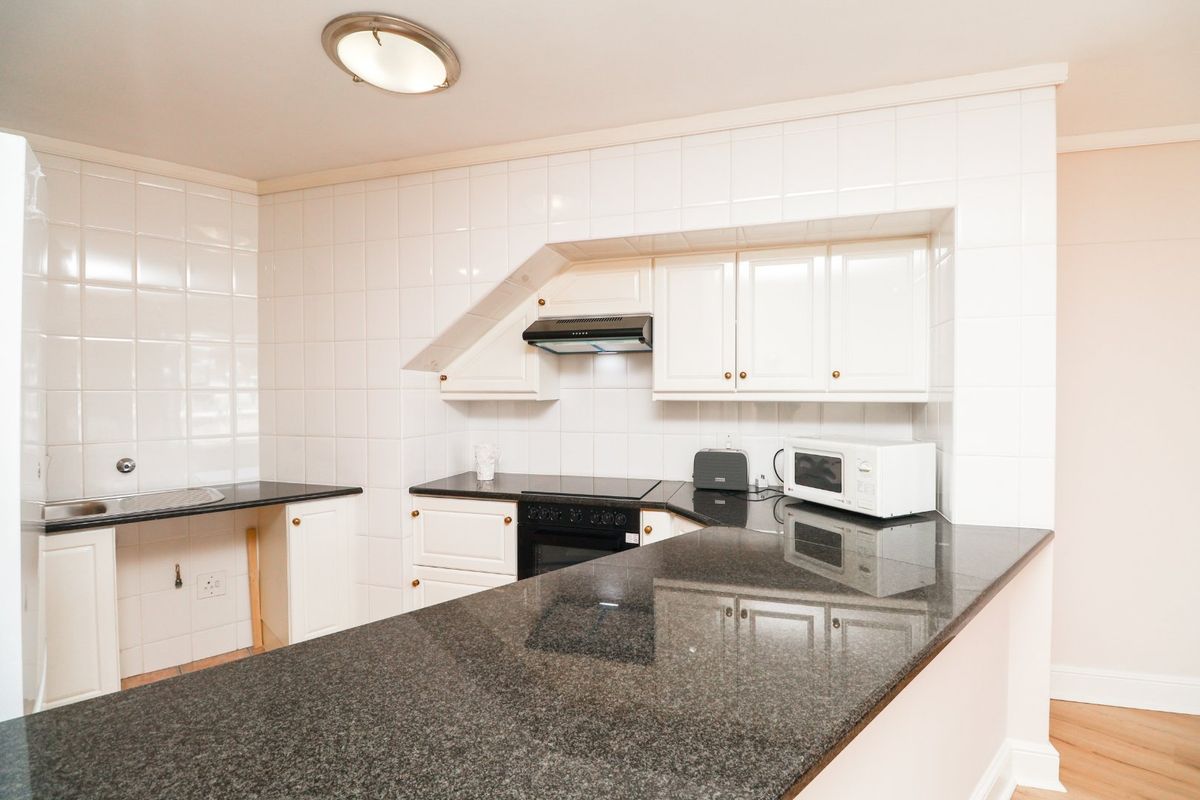 A functional kitchen featuring dark granite countertops, white cabinetry, tiled walls, and a built-in oven with an extractor fan.