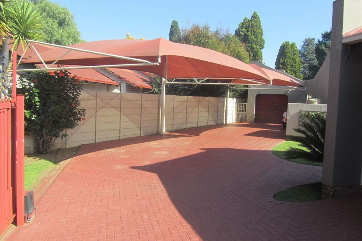 A paved driveway featuring a large shade sail carport structure and access to a garage, set within a fenced residential property.