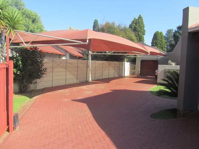A paved driveway featuring a large shade sail carport structure and access to a garage, set within a fenced residential property.