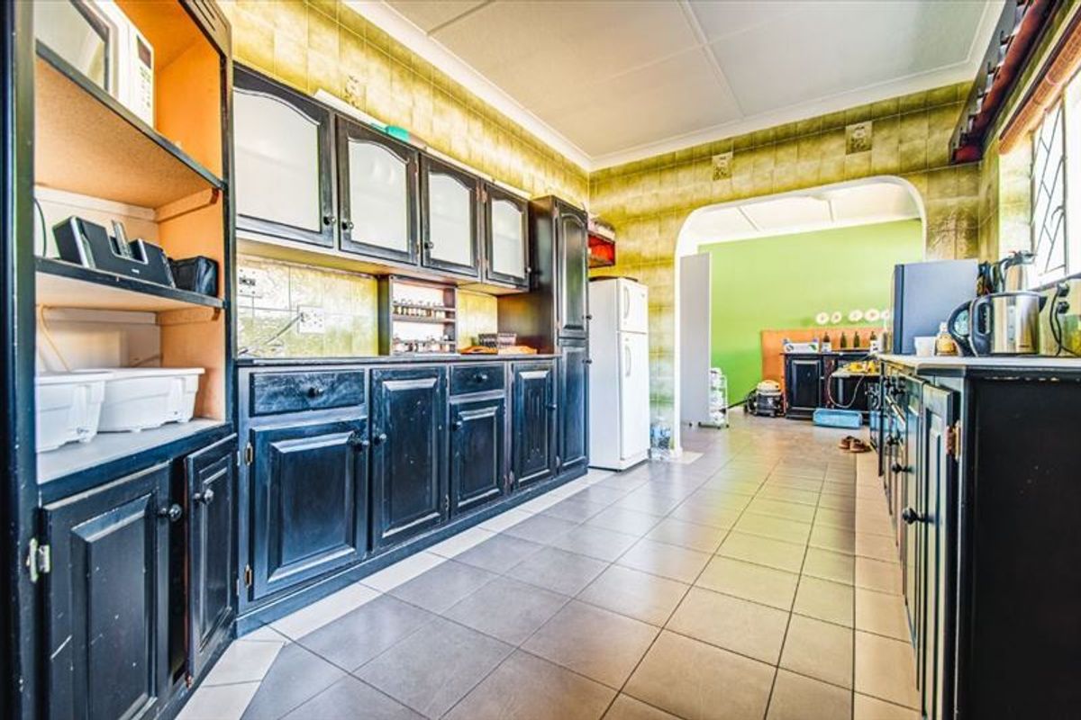 A functional kitchen featuring dark built-in cabinetry, tiled backsplash, and tiled flooring, leading through an archway into an adjacent room.
